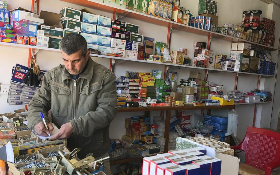 Waad Akram updates a customer's tab in his hardware shop in the Iraqi Christian village of Teleskof on March 24, 2017. Families that fled the Islamic State advance in August 2014 are finally returning to the village and need the goods Akram sells to begin repairs to their damaged homes.