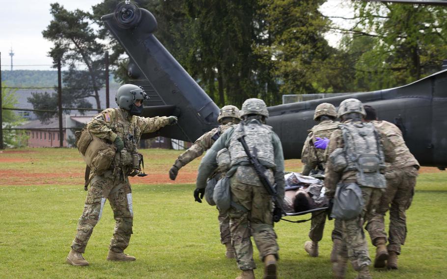 A 12th Combat Aviation Brigade Black Hawk helicopter crew member directs 5th Battalion, 7th Air Defense Artillery Regiment soldiers carrying a simulated casualty during an exercise at Rhine Ordnance Barracks, Germany, on Thursday, May 11, 2017.