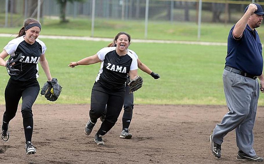 Zama's Paris Hingel, left, clutches the ball after making the catch for the final out against Yokota, and joins teammate Danielle Cruz in celebration as umpire Kelly Cook holds the out call after Tuesday's triple-elimination game in the Far East Division II Softball Tournament. The Trojans edged the two-time defending champion Panthers 15-13 and again later 9-8 to reach the tournament final, needing only one win to secure their first title since 2012. DAVE ORNAUER/STARS AND STRIPES