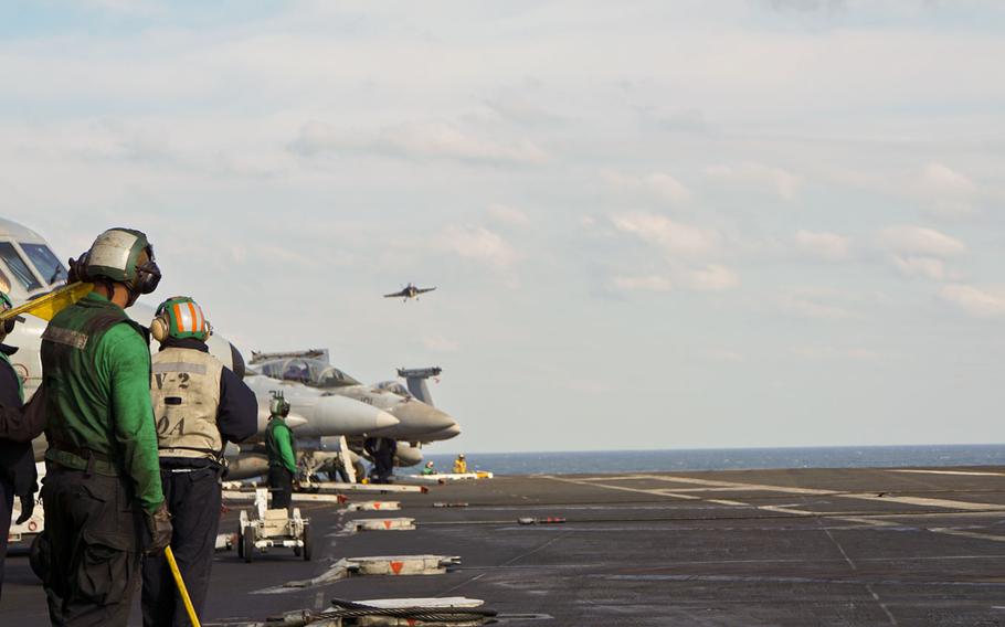 Green-shirted hook-runners, who ensure the arresting cable is reset for each aircraft, wait for a jet to land on the USS Nimitz during a rare tri-carrier exercise near the Korean Peninsula, Monday, Nov. 13, 2017.