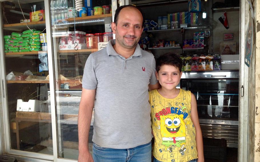 Ahmed Abu Alaa stands with his son Alaa in front of his grocery store in the center of the Syrian capital. Abu Alaa said he was considering expanding the shop to cater to the foreign students he expects will return to Damascus when the war ends.