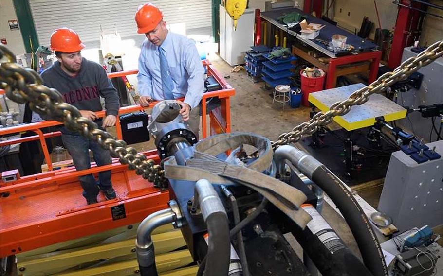 Richard Christenson, right, a civil and environmental engineering professor, and Michael Harris, a doctoral student attach a mounting ring to a hydraulic water pump at a University of Connecticut laboratory.