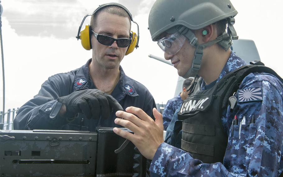 Petty Officer 2nd Class Matthew Spano instructs a member of the Japan Maritime Self-Defense Force member during a live-fire exercise aboard the guided-missile cruiser USS Antietam, Wednesday, Aug. 15, 2018.