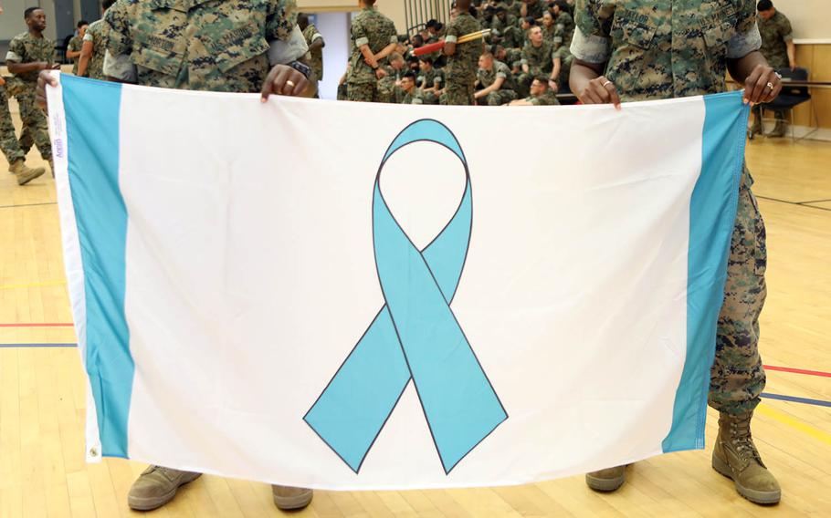 Marines hold up a banner featuring a Sexual Assault Prevention and Response ribbon at Camp Johnson, N.C., April 27, 2018.