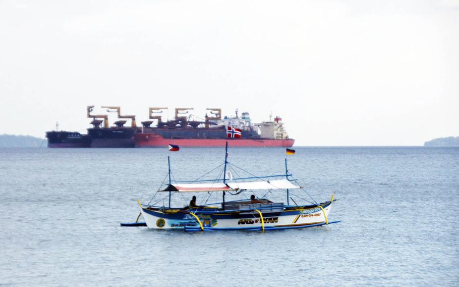A tourist boat drifts in front of a massive commercial vessel near Baloy Beach in Subic Bay, Philippines, in March 2015.