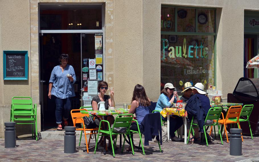 People enjoy something to drink at a cafe with colorful tables and chairs in old town Bayeux, France.