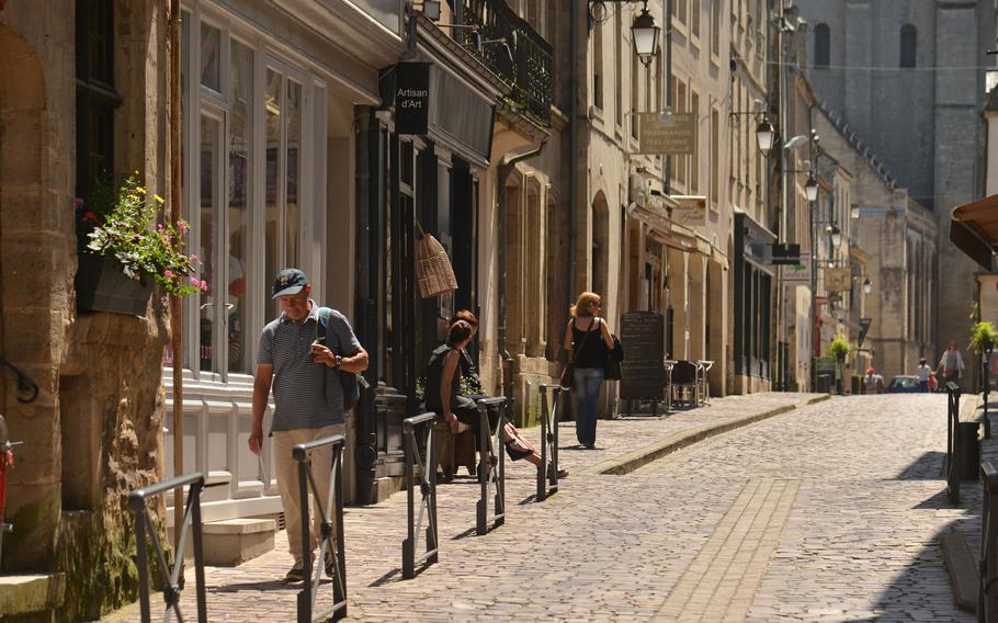 People walk up the cobblestoned Rue des Cuisiniers in the old Normandy city of Bayeux, as a pair of shopkeepers have a conversation.