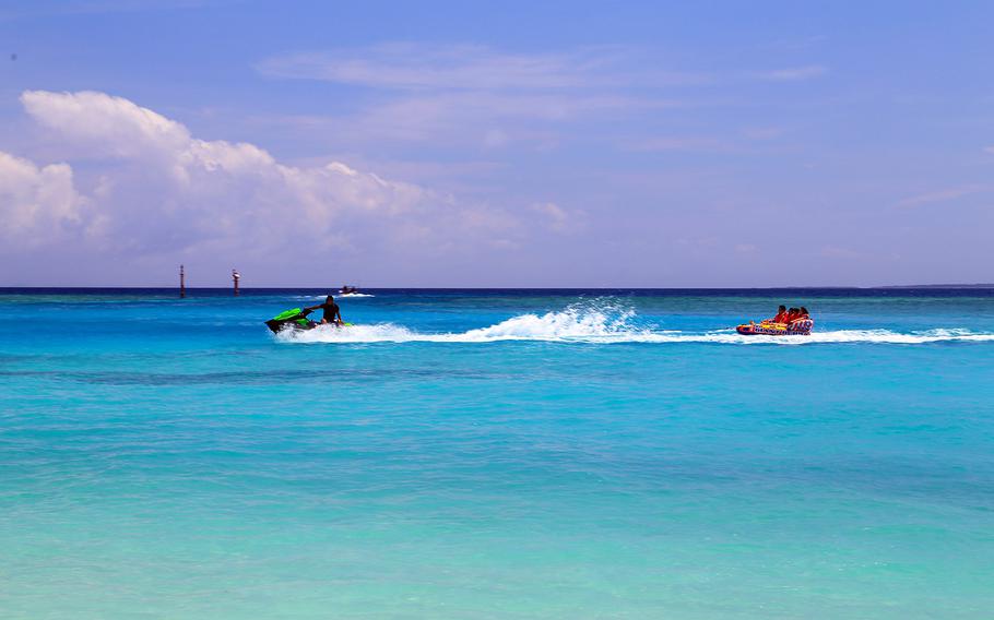 A jet skier speeds over the water while towing people on a float just off Minnajima, Okinawa.