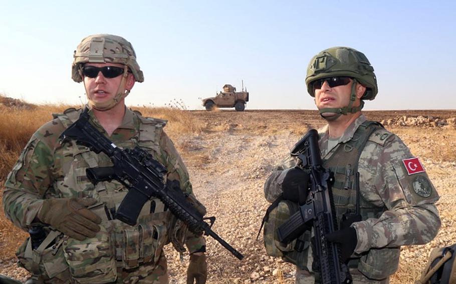 A U.S. servicemember and a Turkish soldier near the Turkish-Syrian border during the third joint ground patrol in Syria Friday, Oct. 4, 2019.