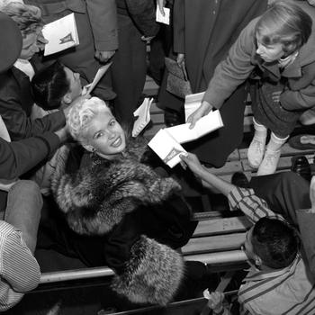 Jayne Mansfield looks up at the photographer as she signs autographs for gathered fans at the Frankfurt Football Stadium, Oct. 5, 1957. 