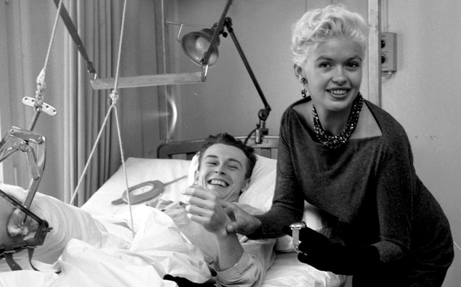 Jayne Mansfield climbs pretends to take the pulse of one lucky soldier while visiting the wards of the Army’s 97th General Hospital in Frankfurt, Germany Oct. 5, 1957. The photographer identified the patient as Kissane (last name only).