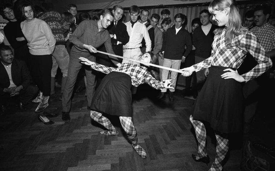 Nancy Wallace eases her way under the limbo bar, one end of which is being held by similarly-attired Christine Jarvis, in the International Grill and Discotheque at the U.S. military's Garmisch Recreation Area in Germany,  December 1965. 