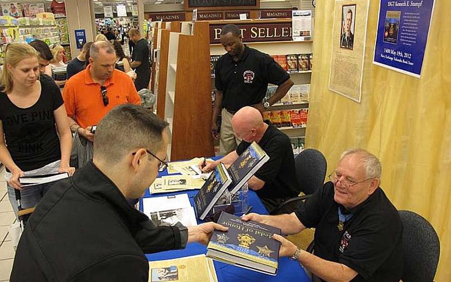 Medal of Honor recipients Ken Stumpf, sitting in foreground, and Don Jenkins, sign autographs at the Yokosuka Navy Exchange on May 19, 2012. Each man received the award after saving the lives of their comrades during the Vietnam War.