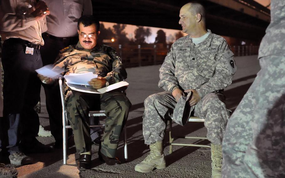 Iraqi army Lt. Col. Abadi Mashkoor Sultan, commander of 1st Battalion, 56th Baghdad Brigade, left, looks at photos from a previous meeting, brought to him by Lt. Col. Gregory McVay, right, security director for the 72nd Joint Area Support Group-Central. The evening meeting to talk about security issues in the International Zone took place on a bridge spanning the Tigris river that connects Baghdad's Red Zone with the IZ, formerly known as the Green Zone. McVay meets Abadi, who commands all Iraqi army troops in the International Zone, on a regular basis. In the background is the 14th of July Bridge.