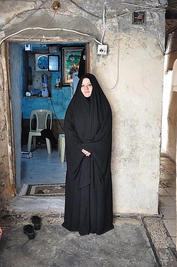 Aklas Farhood, whose husband was killed in a Baghdad bombing, stands in front of the tiny room that she lives in with her two sons.