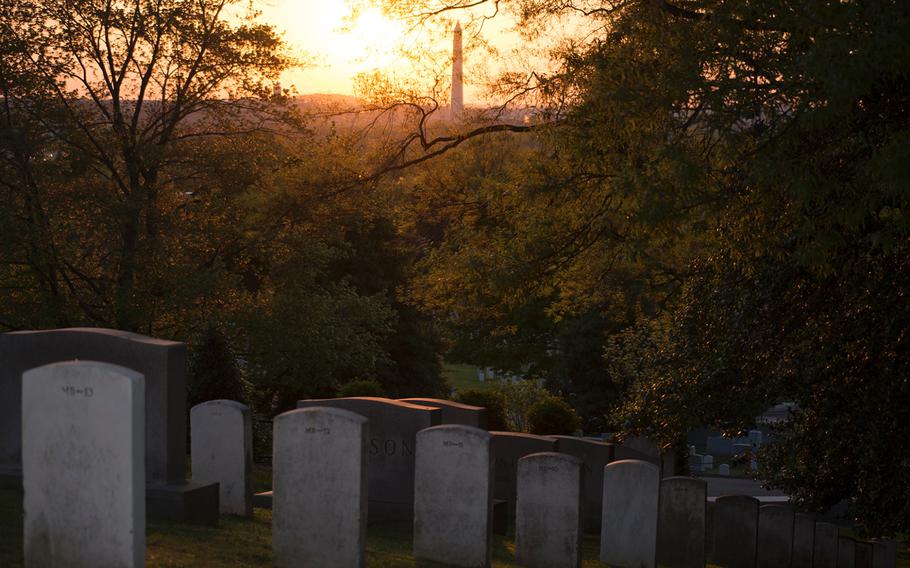 The sky is cast in brilliant yellows and pinks as the sun rises over Arlington National Cemetery on May 4, 2014. The Washington Monument is seen through the trees. 