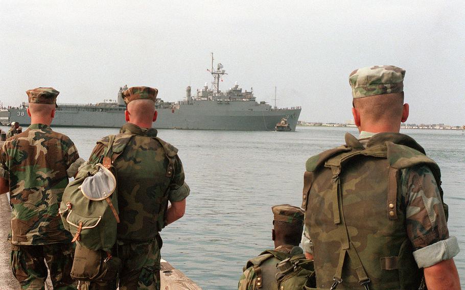 U.S. Marines watch from a pier as the dock landing ship USS Pensacola is assisted by a tug. Elements of the 2nd Marine Division embarked aboard the Pensacola and other ships to participate in Operation Desert Shield. U.S. Marine Corps photo by Gunnery Sgt. R.L. Jaggard