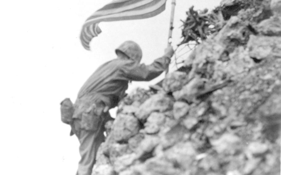 Braving sniper fire, Marine Lt. Col. Richard P. Ross, Jr., places the American flag on a parapet of Shuri castle on Okinawa.  This 1st Marine Division flag was the first to be raised over Cape Gloucester and Peleliu by that unit. The metal staff to which the flag is attached had been used for Japanese ensigns and bears the marks of American shell fire.