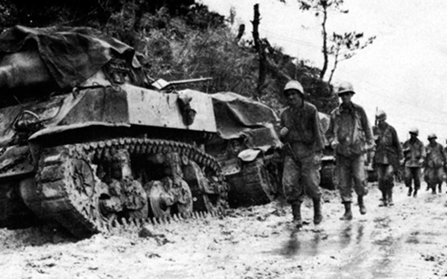 Infantrymen from the 77th Division trudge toward the front lines past mud-clogged tanks and mud and heavy rains increased the difficulties of fighting on Okinawa. 
