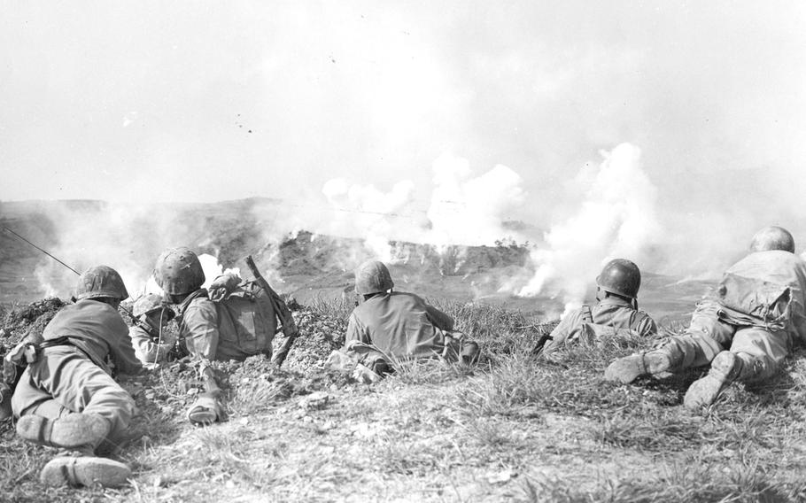 Two days after the victory in Europe was celebrated, 1st Division Marines  wait on the crest of a slope while a barrage of phosphorous shells explodes among the Japanese positions on the farther incline during their drive toward Naha, the capital city of Okinawa.