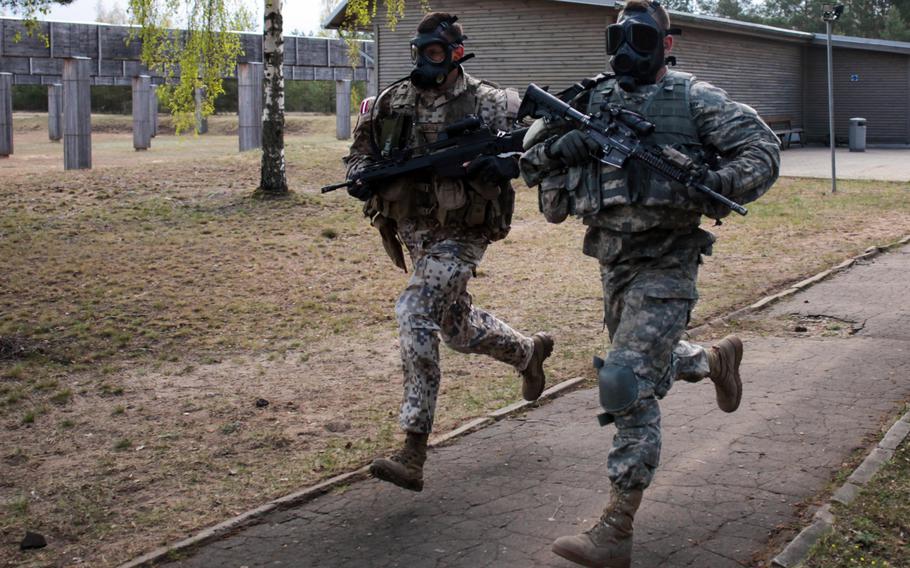 An American and a Latvian soldier sprint in full gear and gas masks at the start of a stress shooting competition on Wednesday, April 30, 2014, meant to build camaraderie and test their endurance and marksmanship under simulated battlefield conditions.