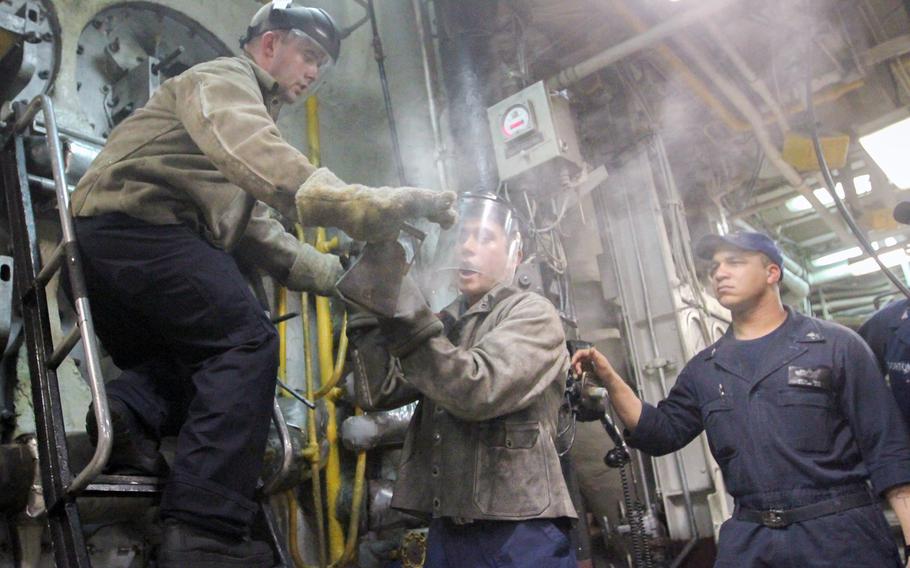 Seaman Nathaniel Post, left, hands Seaman Chris Rogakos a hot burner barrel from the boiler through a cloud of steam aboard the USS Bataan on July 22, 2014. The two sailors wear fire-resistant jackets, earplugs and masks to protect themselves from the intense heat.