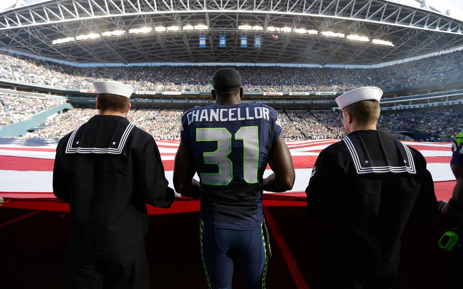 Seattle Seahawks' strong safety Kam Chancellor (31) stands with military service members holding a giant U.S. flag before an NFL football game between the Seattle Seahawks and the Minnesota Vikings, Sunday, Nov. 17, 2013, in Seattle. 