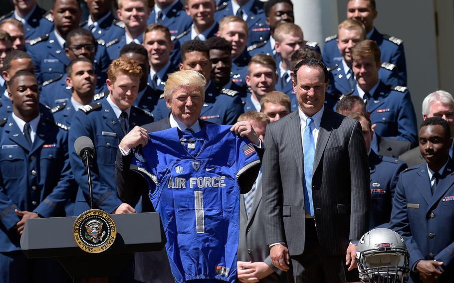 President Donald Trump holds up an Air Force Academy football team jersey in the Rose Garden of the White House on Tuesday, May 2, 2017, during a presentation ceremony of the Commander-in-Chief trophy to the Air Force Academy football team. At right is U.S. Air Force Academy football team coach Troy Calhoun. 