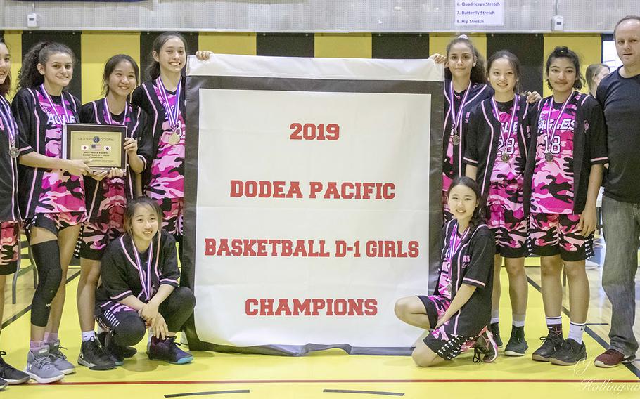 American School Bangkok's girls players and coach David Lucas gather round the banner. It's their third straight in the Far East Division I tournament.