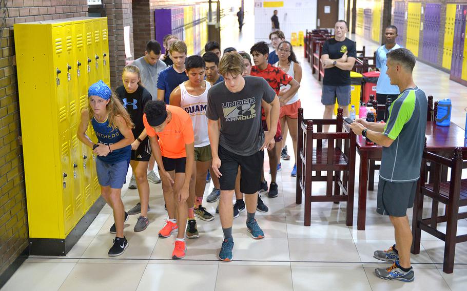 Coach Josh Dinkler gets set to start his stopwatch as members of the Bahrain cross country get set for a run around the school's hallways on Thursday, Oct. 3, 2019. The team trains before school starts to avoid heat-related injuries. 