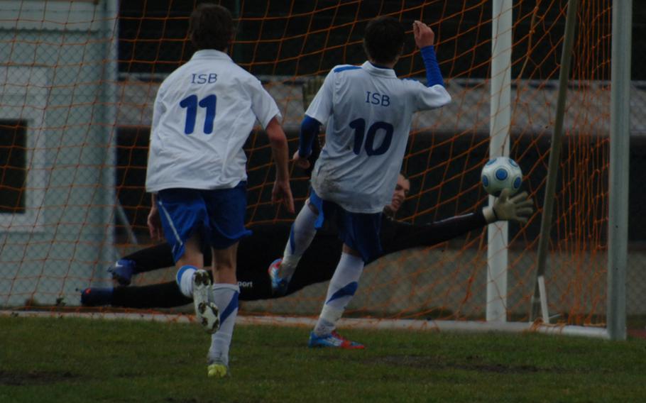 Ramstein goalkeeper Cody Collins stretches out to make one of his five saves in a 3-1 loss Friday to visiting International School of Brussels on a shot by ISB’s Lucas McNaughton. Trailing the play is ISB’s Stein Kruiderein.  