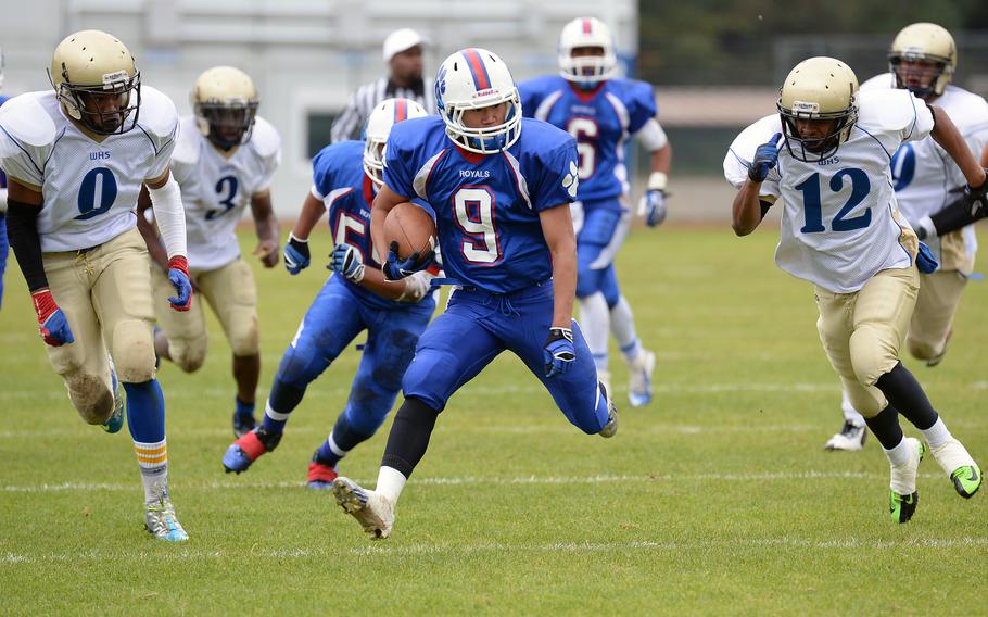 Ramstein's Young Jae Oh picks up a big gain as Wiesbaden's Andrew Murray, left, and Carlos Grinter close in. The Royals beat Wiesbaden 20-7, Saturday, Oct. 12, 2013.