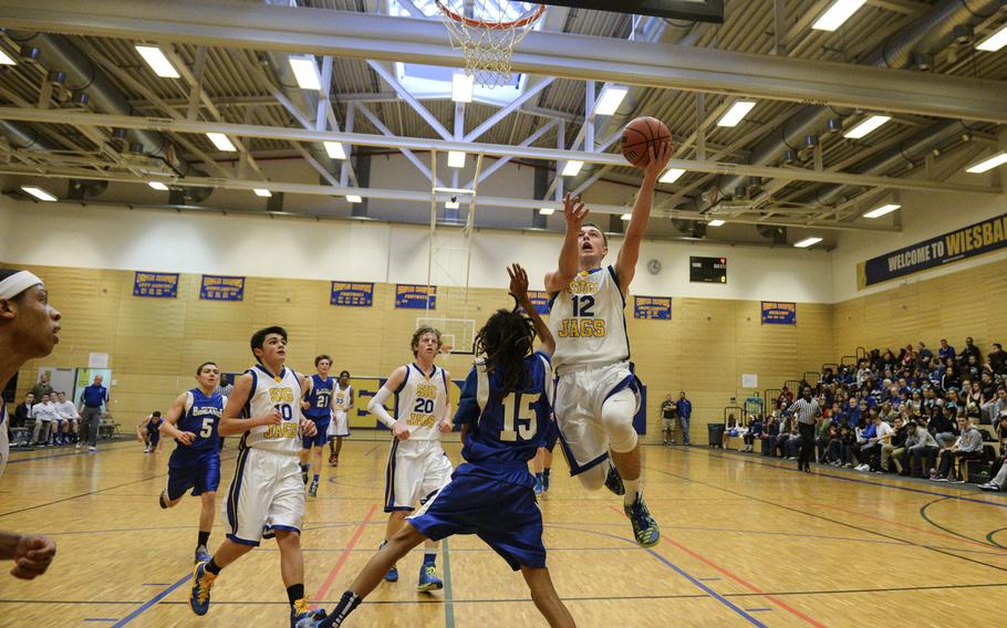 Sigonella's Jason Berlin finishes a fast break layup over a Brussels' Aaron Richardson in the semifinals of the DODDS-Europe tournament, Friday, Feb. 20, 2015.