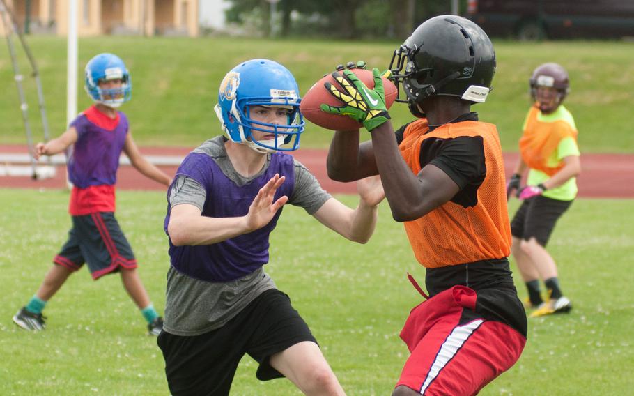 Hohenfels' Trey Briscoe catches a pass while Ansbach's Gary Smith reaches in for the two-hand touch during a football camp held at Ansbach, June 13, 2015. 