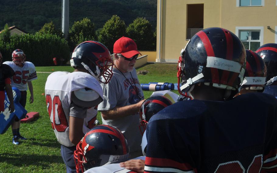 Senior quarterback Hayden Roers, left, and the rest of the first-team offense listen to head coach Rick Dahlstrom describe a play for the Aviano Saints during a recent practice.
