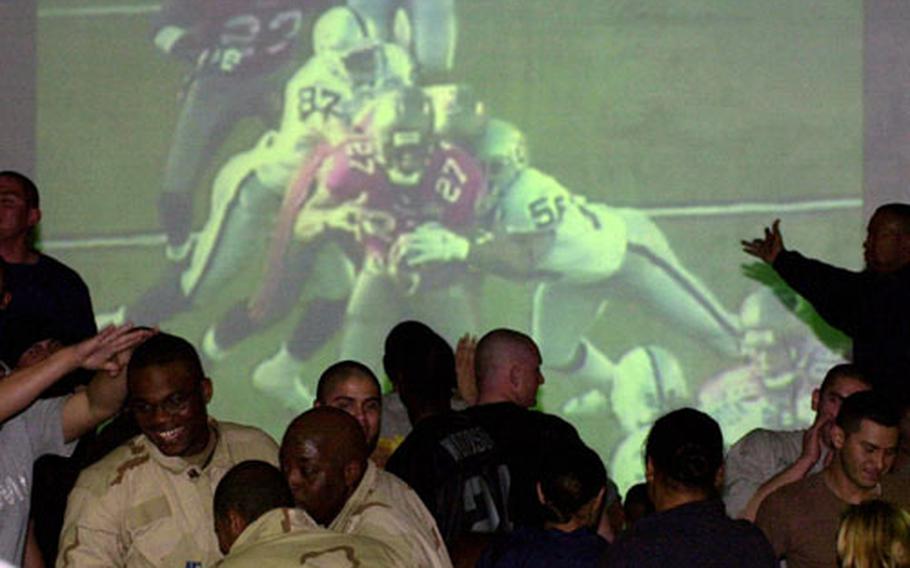 Soldiers at Camp Doha react to the action during Super Bowl XXXVII, broadcast on a big-screen at a former warehouse turned into the base club.