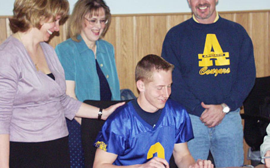 Flanked by his mother, Lisa, left; Ansbach principal Jennifer Rowland, center; and head football coach Marcus George, Garrett Eichhorn of Ansbach High School prepares to sign a letter of intent to play football for the University of Dubuque in Iowa during a ceremony Friday at Ansbach, Germany.