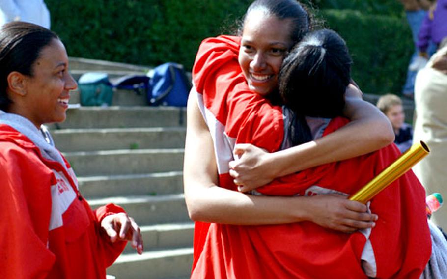Kaiserslautern High School 1,600 sprint medley runners Mandra Smith, left, and Dupe Babatunde, right, congratulate teammate Cassie Freeman after her final sprint gave the Raiders the gold medal.
