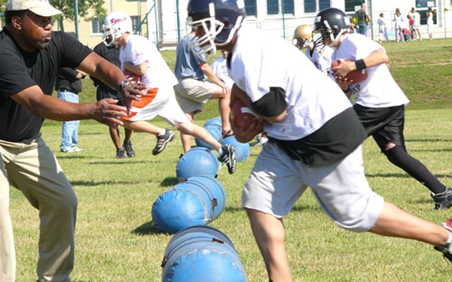Volunteer staffer Jim Lynch of Hanau helps Bitburg&#39;s Corey Legister through a drill for running backs Wednesday on the first day of the DODDS-Europe football camp.