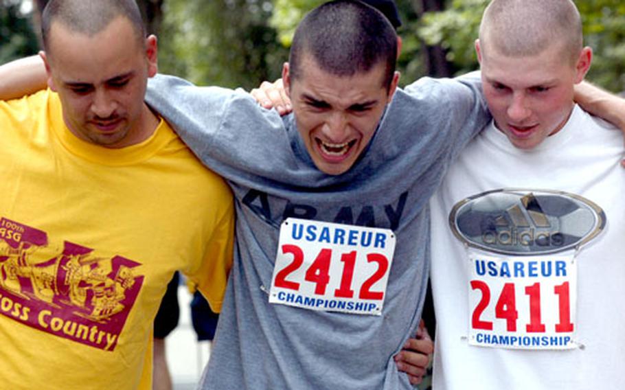 Spc. Nick Ramirez grimaces against the pain of a cramped thigh muscle as Staff Sgt. Miguel Hidalgo, left, and Sgt. George Hayden help him away from the finish area of the Army 10-Miler European qualifier.
