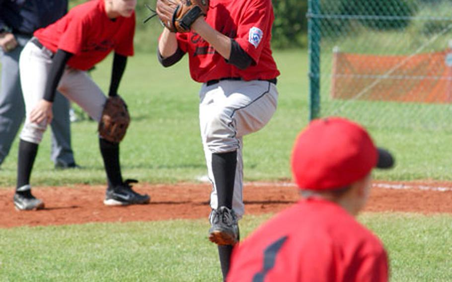 Dustin Bratcher of East Anglia, England, winds up to throw a pitch against Arabian-American. In the foreground is East Anglia third baseman T.J. Klein, and in the background playing first base is Caleb Nelson.