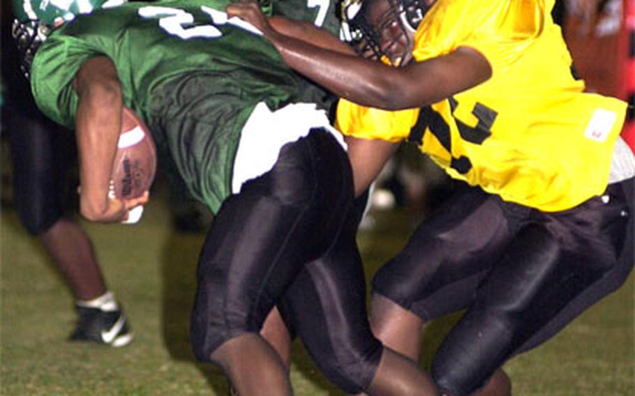 Kubasaki’s Lenard White (26) gets dragged down by Dominique Jernigan (72) of the Kadena Panthers.