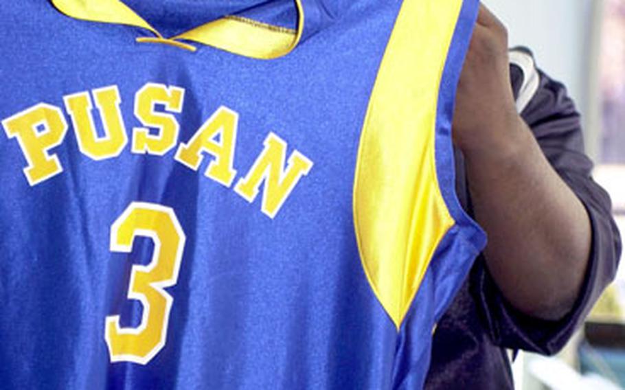 Phillip Loyd, coach of the Pusan American boys basketball team, displays a jersey with a small white patch denoting the school’s 38-year history.