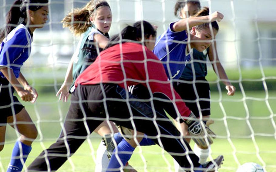 Guam goalie Jamie Bartnik, in red shirt, goes after and eventually stops a loose ball in front of her net as teammate Jordan Marquez, right, and Kubasaki&#39;s Kara Koeneke, give chase.