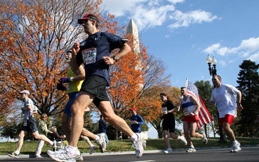 Runners in Sunday&#39;s Marine Corps Marathon pass the Washington Monument on their way to the 14-mile mark, with Mark Clingan of Jacksonville, N.C., carrying the colors.