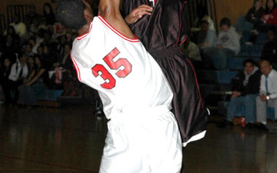 Wilberto Badillo of the Zama American Trojans shoots over Victor Mason (35) of the Nile C. Kinnick Red Devils during Tuesday&#39;s Kanto Plain Association of Secondary Schools/DODDS-Japan Basketball League game at Fleet Gym, Yokosuka Naval Base, Japan.