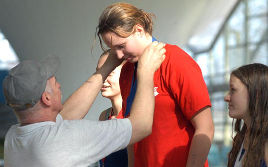 Steve Genter, a three-time swimming medalist in the 1972 Olympics in Munich, gives the first-place medal for the 15 to 16-year-old girls&#39; 100 meter freestyle event to Heidelberg&#39;s Lauren Drake, who set a record.