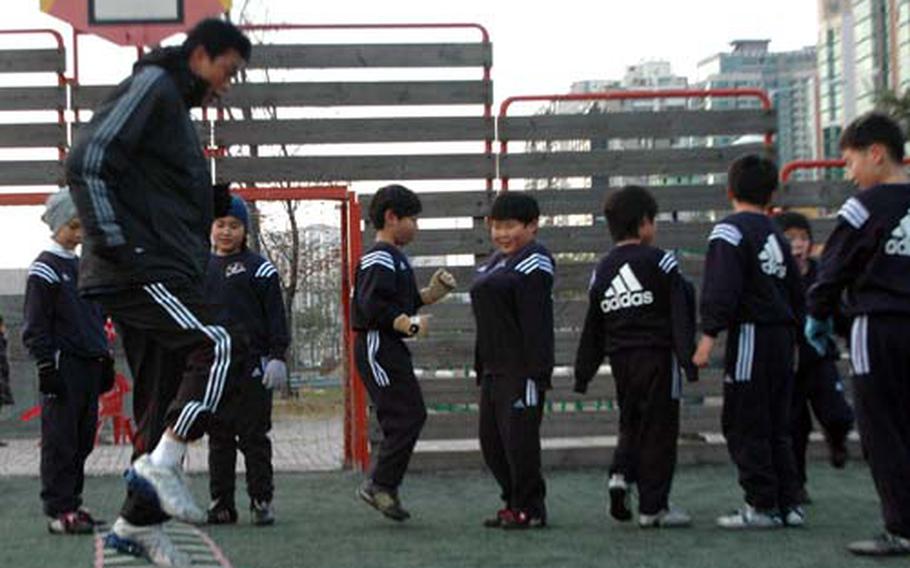 Camille Pereira (in blue hat) watches as her coach, Lee Sang-yoon, demonstrates a drill. Cami says she can follow his directions by watching rather than listening. Lee, who speaks only a little English, said Cami does fine following directions.