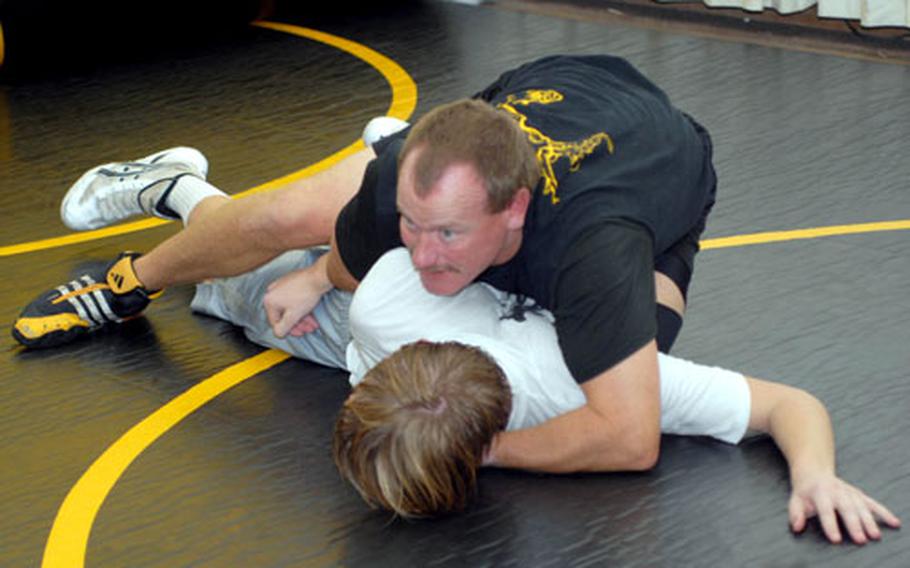 Coach Steve Schrock of the defending Far East High School Wrestling Tournament team champion Kadena Panthers demonstrates technique on sophomore 129-pounder Jacob Bishop during Monday's practice at Panther Pit wrestling annex at Kadena High School. Bishop is a transfer from Zama American and last year's 129-pound runner-up.