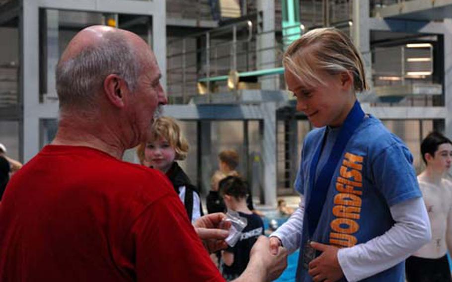 Hallie Kinsey, 8, of Sigonella, Italy, receives her sixth gold medal, this one for her league-record-breaking 50-meter butterfly race, by 1972 Olympic gold medalist (4x200-meter freestyle relay) Steve Genter at the 2009 European Forces Swim League Championships at Berlin’s Europa Sportpark Sunday. Kinsey set records in every race she swam.